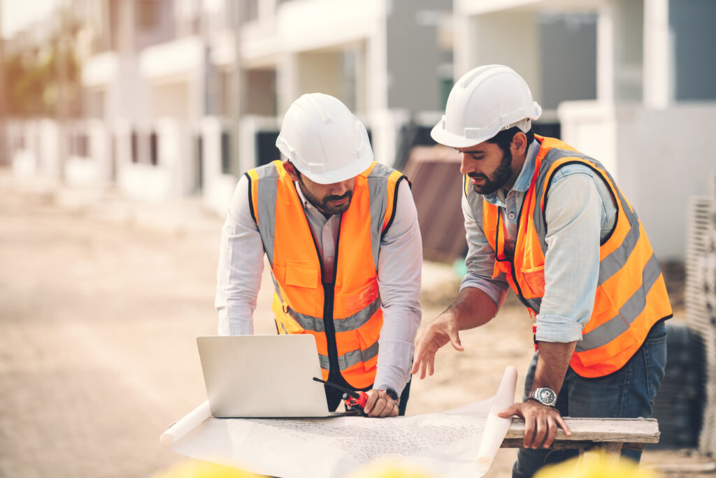 Profissionais de construção civil a analisar planta e portátil no estaleiro